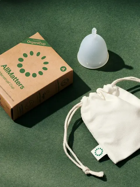Menstrual cup with box and drawstring pouch on green background.