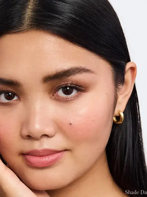 Close-up of a person with smooth skin, wearing gold hoop earrings. Text: "Shade Dark".