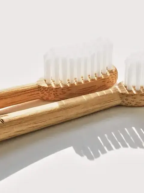 Two bamboo toothbrushes with white bristles on a light background.
