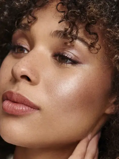 Close-up of a person with curly hair and glowing skin, looking to the side.