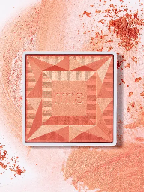 Coral blush compact with "rms" embossed, surrounded by scattered powder.