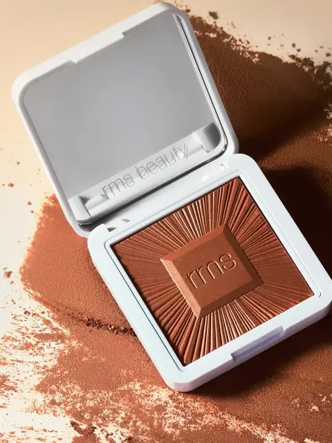 Open compact of rms beauty bronzer with embossed design on scattered powder.