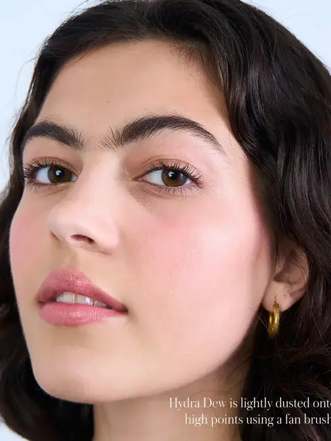 Woman with glowing skin, wearing gold hoop earring. Text: "Hydra Dew is lightly dusted...