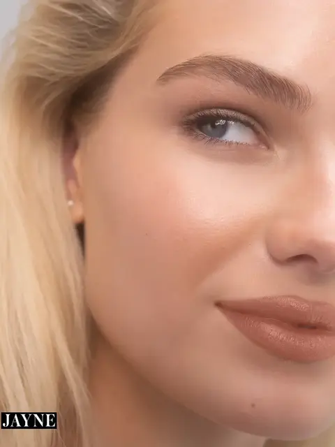 Close-up of a woman's face with smooth skin and nude lipstick. Text: "JAYNE".