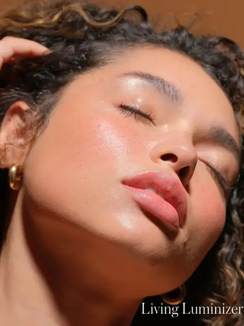 Person with glowing skin, eyes closed, wearing gold hoop earrings. Text: "Living Luminizer".