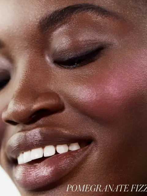 Close-up of a smiling person with pink blush. Text: "Pomegranate Fizz".
