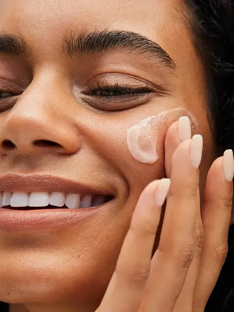 Person applying cream to cheek with fingers.
