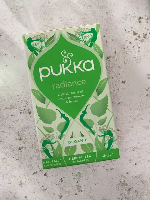 Pukka Radiance herbal tea box on a textured surface, featuring nettle, peppermint, and fennel.