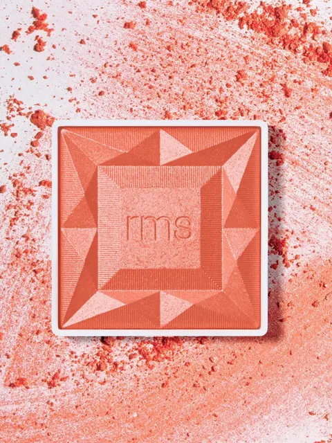 Coral blush compact with "rms" logo, surrounded by scattered powder.