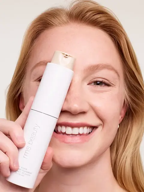 Smiling person holding rms beauty foundation bottle.