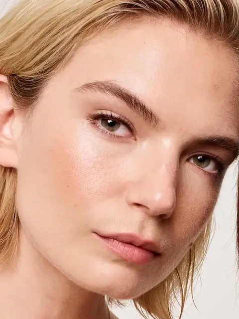 Close-up of a person with clear skin and light hair, looking towards the camera.