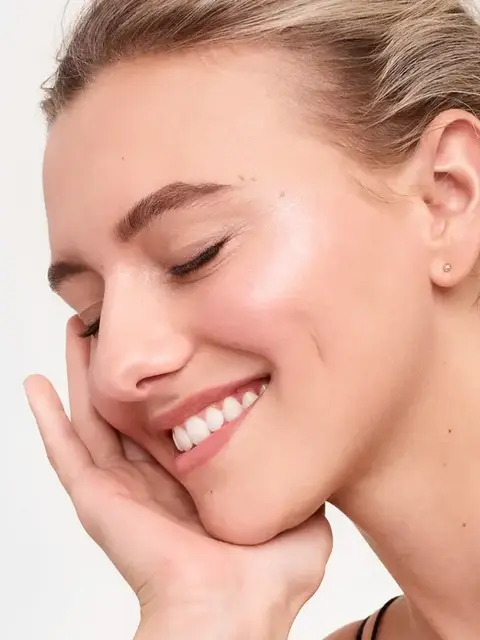 Woman with closed eyes smiling, touching her cheek.