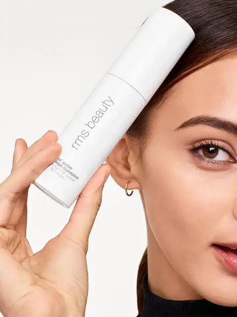Woman holding rms beauty foundation bottle near face.