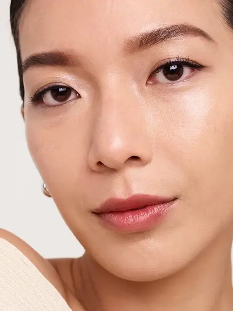Close-up of a person with smooth skin and natural makeup, wearing a beige top.