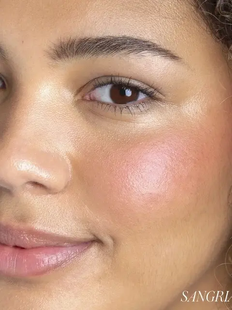 Close-up of a person's face with glowing skin and pink blush. Text: "SANGRIA".