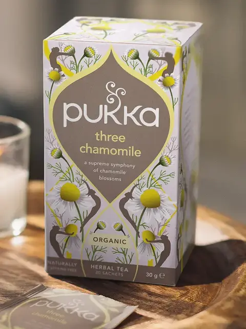 Pukka Three Chamomile tea box on wooden tray, 20 sachets, organic herbal blend.
