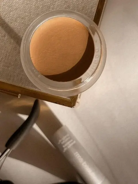 Open jar of beige cream on a table with a tube and tool nearby.