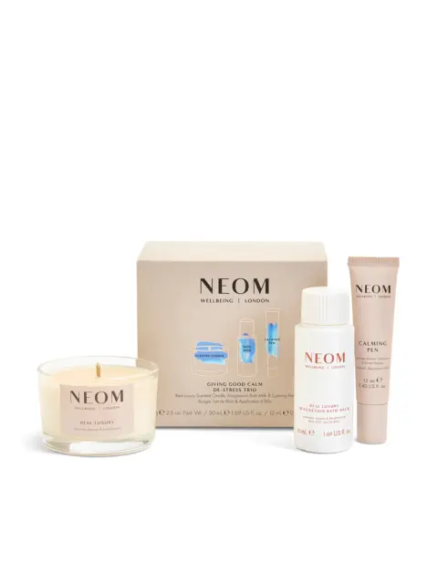 NEOM de-stress trio with candle, bath milk, and calming pen in front of branded box.