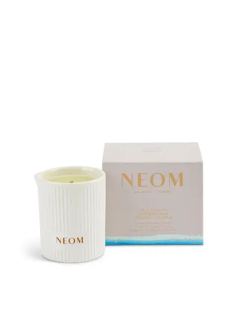 White NEOM candle with ribbed texture next to its box. Text: "Real Luxury Intensive Skin Treatment Candle".