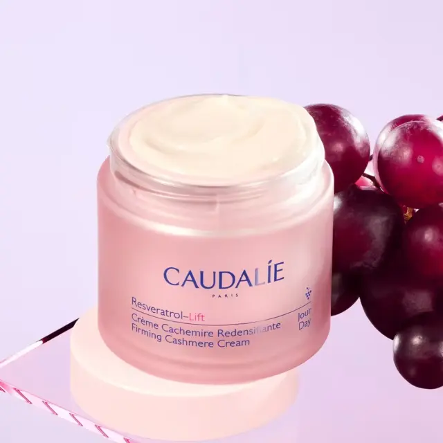 Caudalie Resveratrol-Lift Firming Cashmere Cream jar with grapes on a purple background.