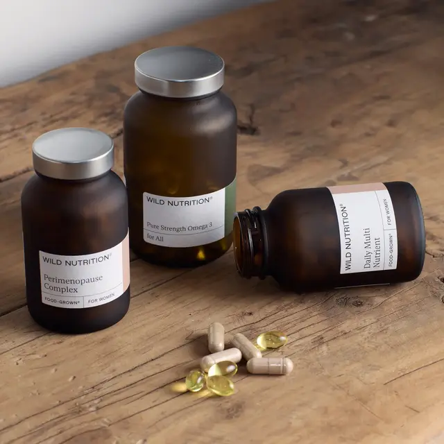 Three brown supplement bottles on a wooden table with capsules and softgels.