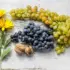 Yellow flowers, green and purple grapes, and walnuts on a rustic wooden surface.