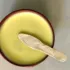 Wooden bowl with yellow balm and a small spatula on a light surface.