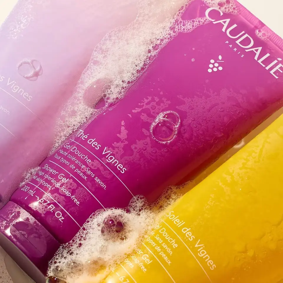 Three Caudalie shower gels in purple, pink, and yellow, covered in bubbles.