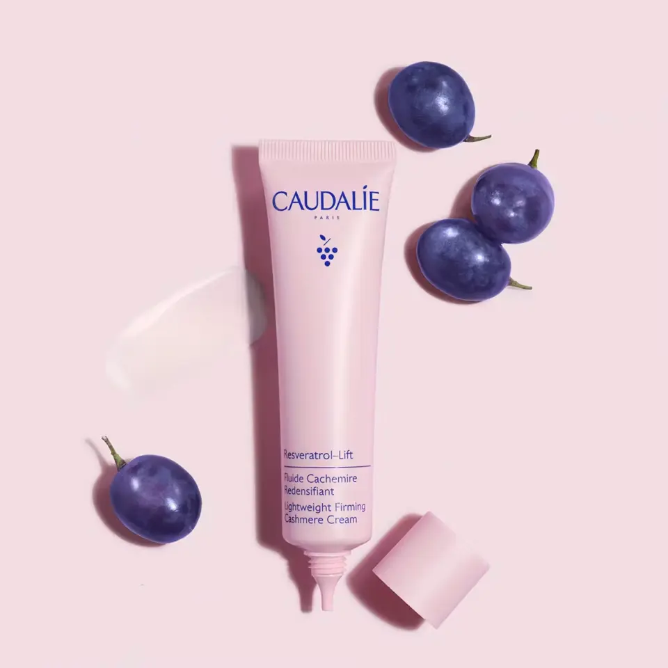 Pink tube of Caudalie cream with grapes on a pink background.