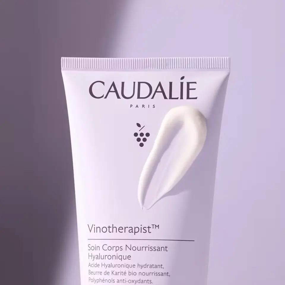 Caudalie Vinotherapist body cream tube with cream smear on a purple background.