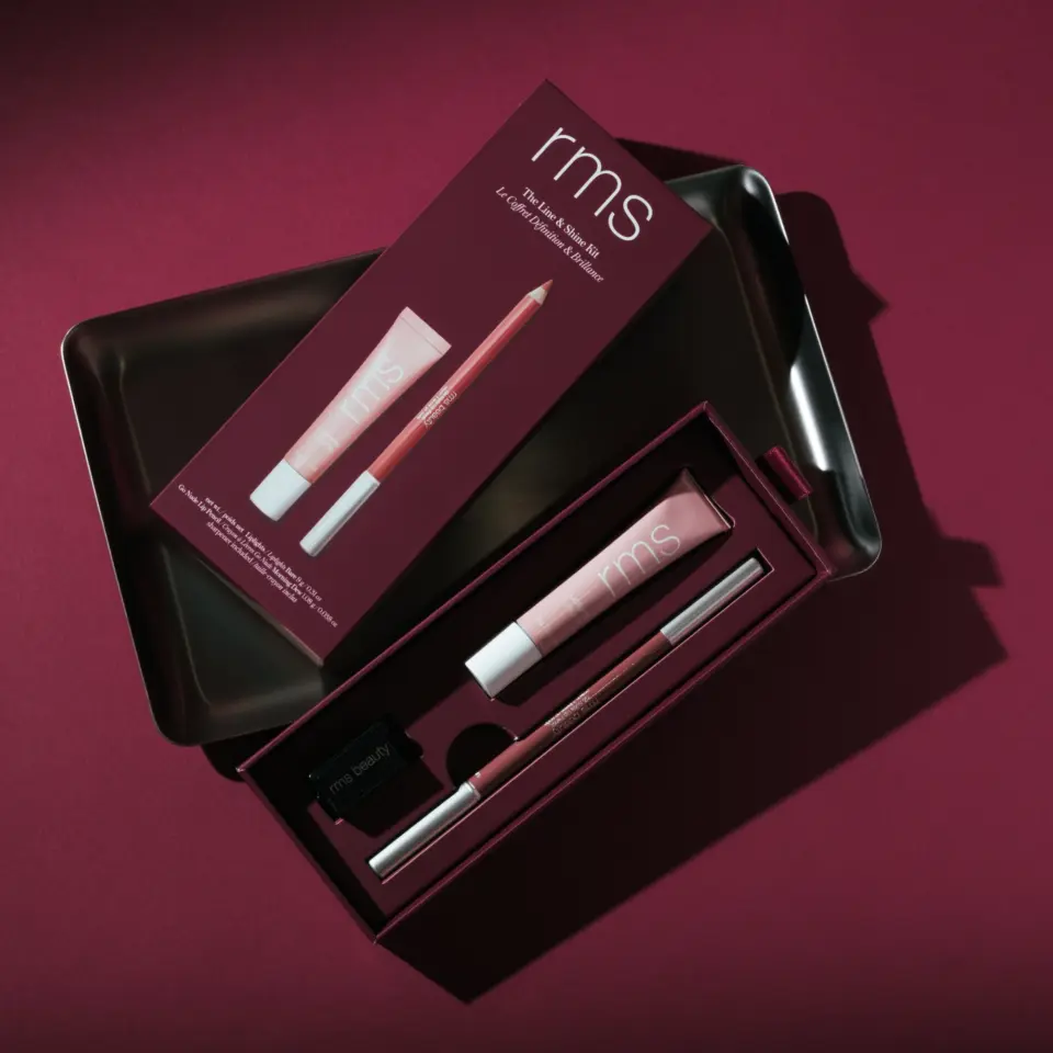 RMS lip kit with gloss, pencil, and sharpener in a dark red box on a matching background.
