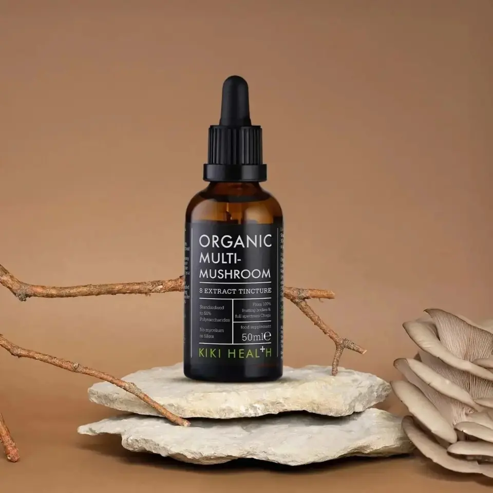 Organic Multi-Mushroom tincture bottle on stone with branches and mushrooms.