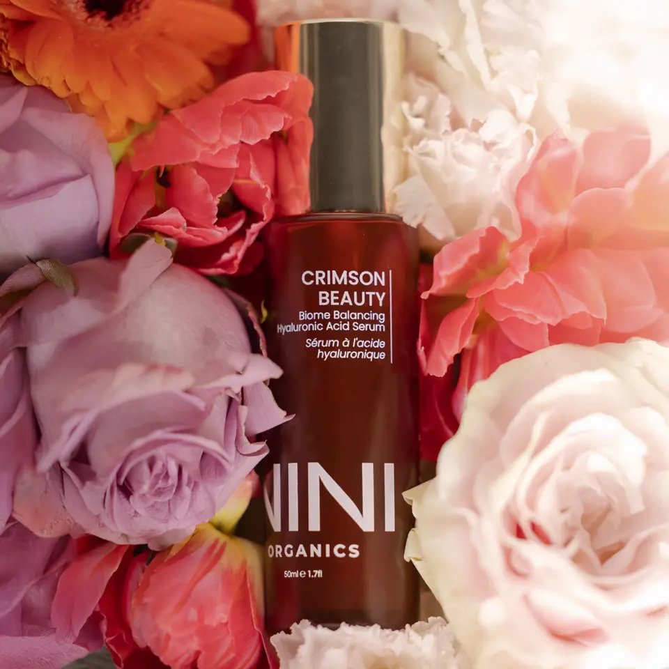 Crimson Beauty serum bottle surrounded by colourful flowers.