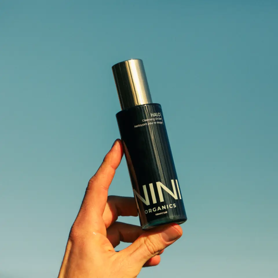 Hand holding NINI Organics bottle against a clear blue sky.