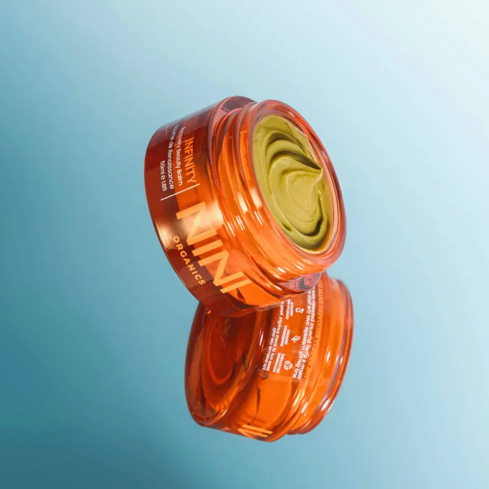 Orange jar of green skincare cream on a reflective surface.