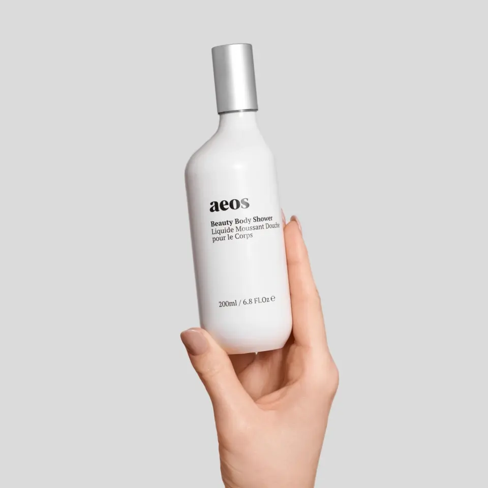 Hand holding aeos Beauty Body Shower bottle, 200ml, on grey background.
