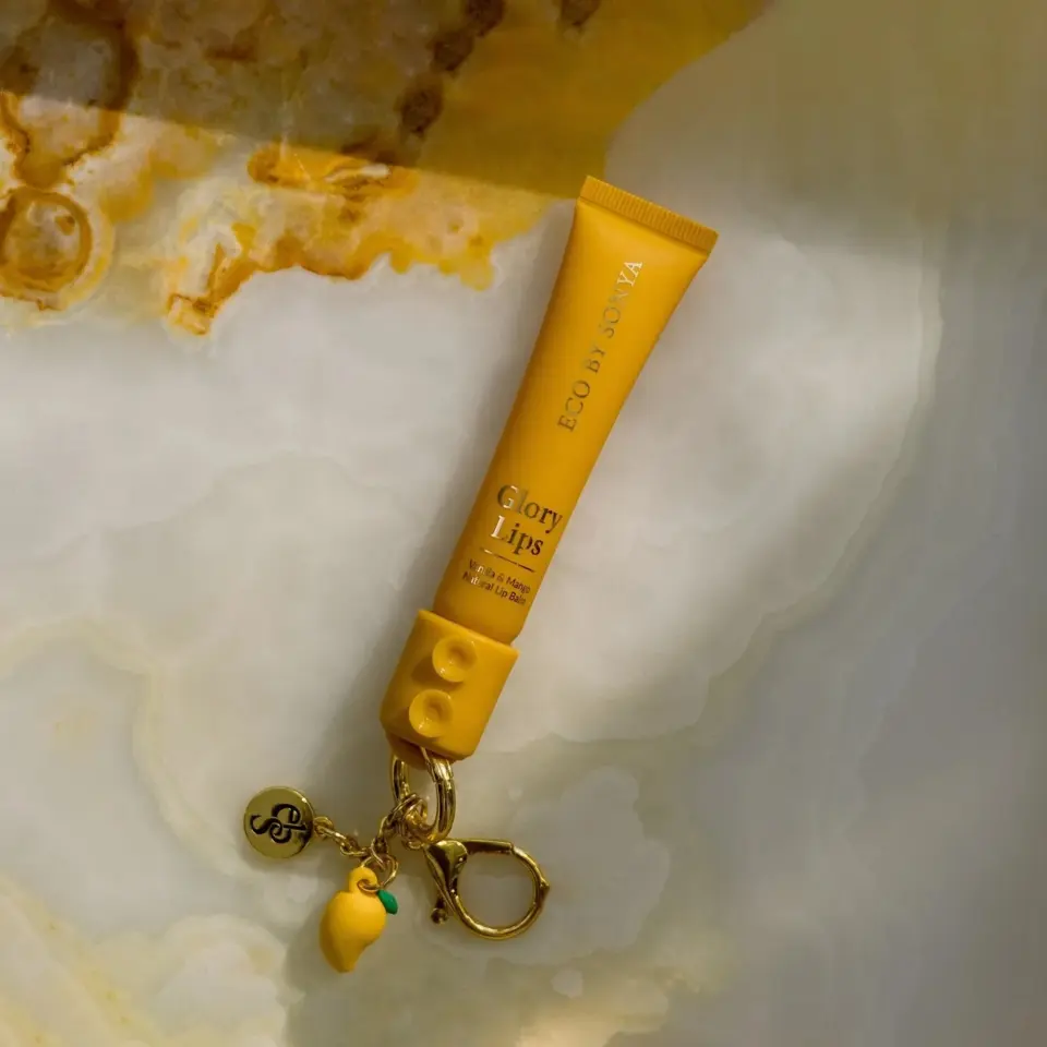 Yellow tube of Eco by Sonya Glory Lips balm with keychain on marble surface.