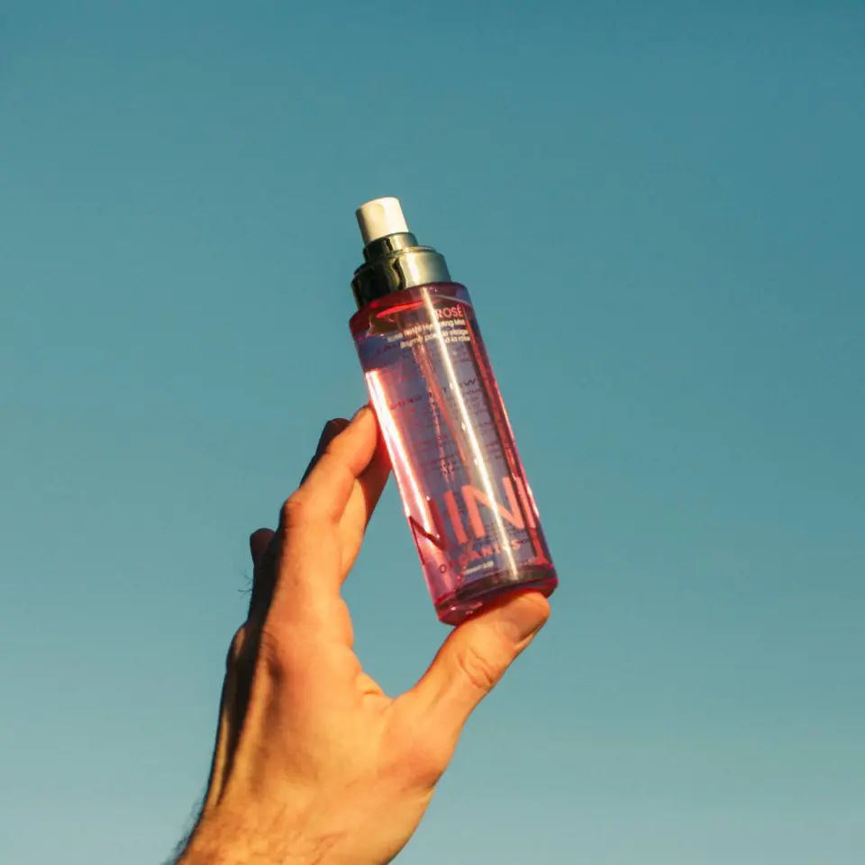 Hand holding a pink spray bottle against a clear blue sky.