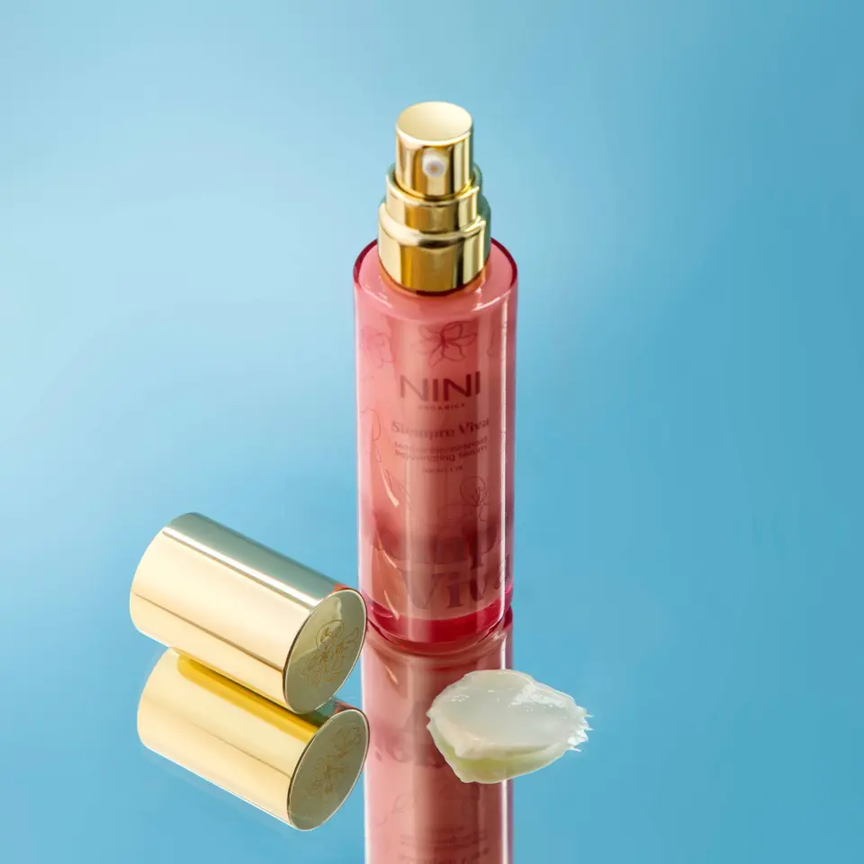 Red spray bottle with gold cap on blue background, cream smear beside it.