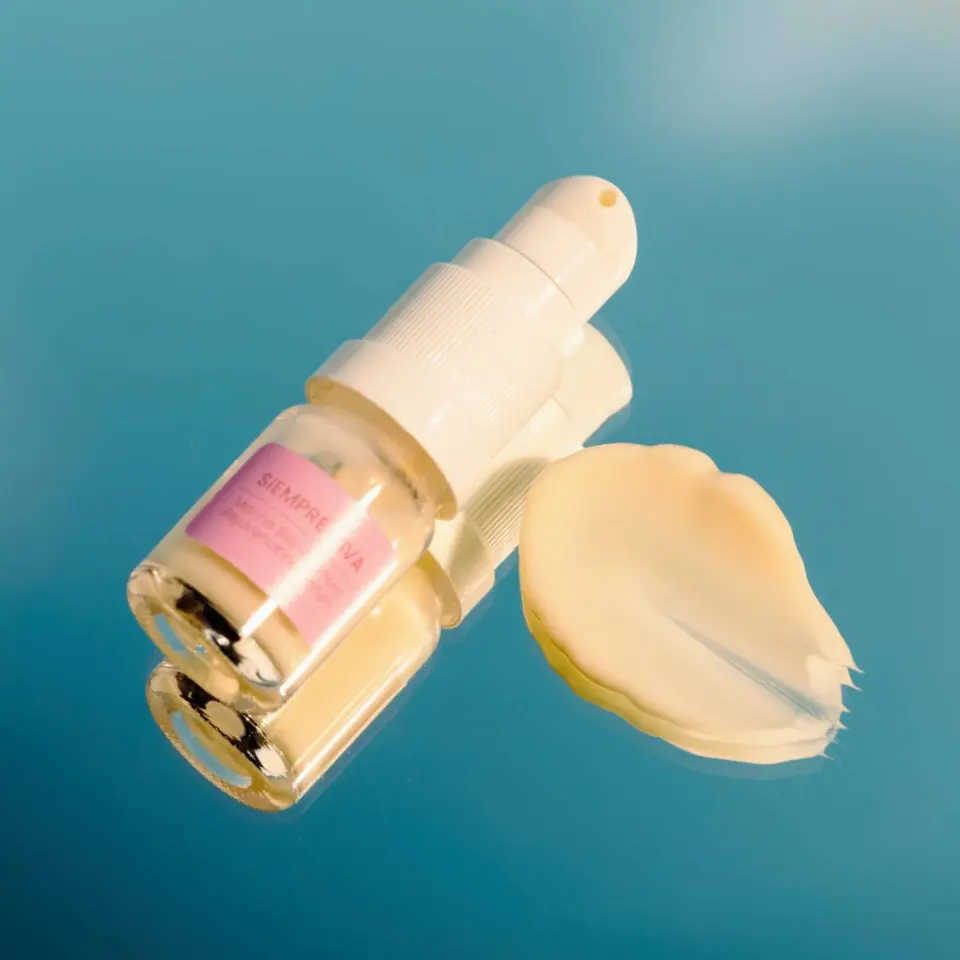 Skincare serum bottle with pump and cream smear on blue background.