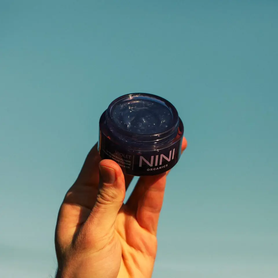 Hand holding a NINI Organics jar against a blue background.
