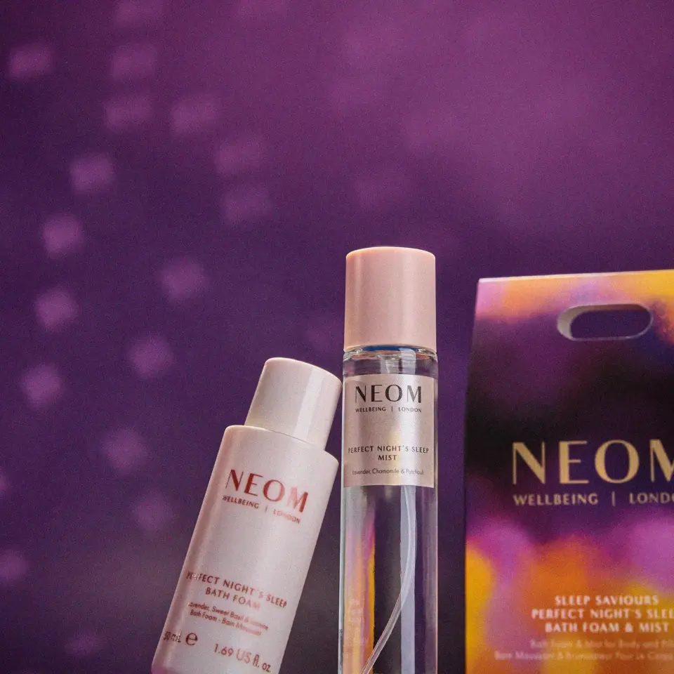 Neom Wellbeing bath foam and mist with packaging on a purple background.