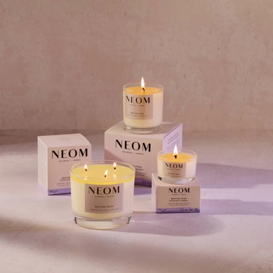 Lit NEOM candles with packaging on a light surface.