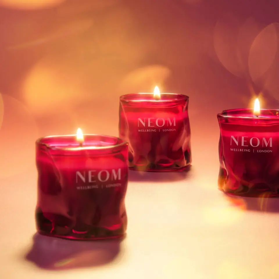 Three lit red candles with "NEOM Wellbeing London" text on a soft-focus background.