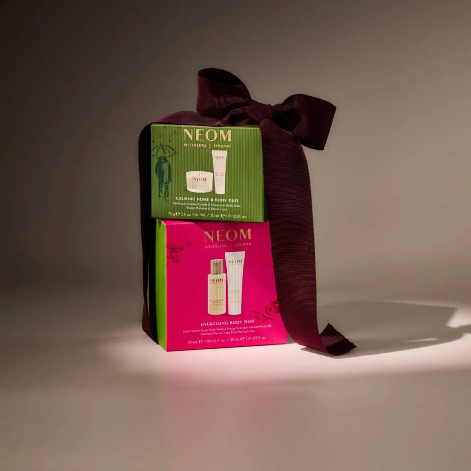 Gift box with NEOM skincare products, green and pink packaging, tied with a dark purple ribbon.