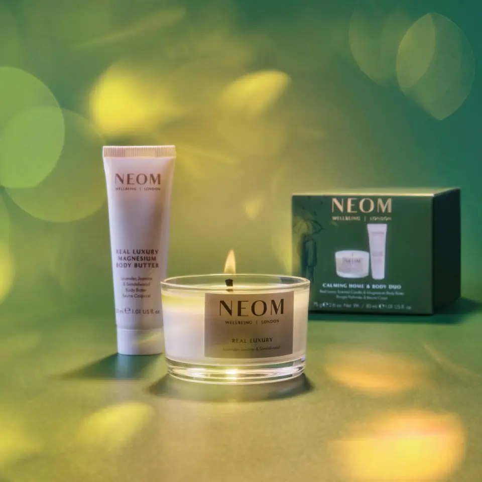 Neom candle, body butter, and gift box on a green background with soft light effects.