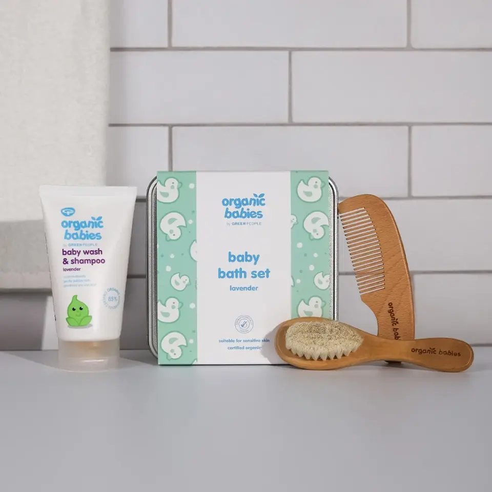 Baby bath set with lavender wash, wooden comb, and brush on a tiled background.