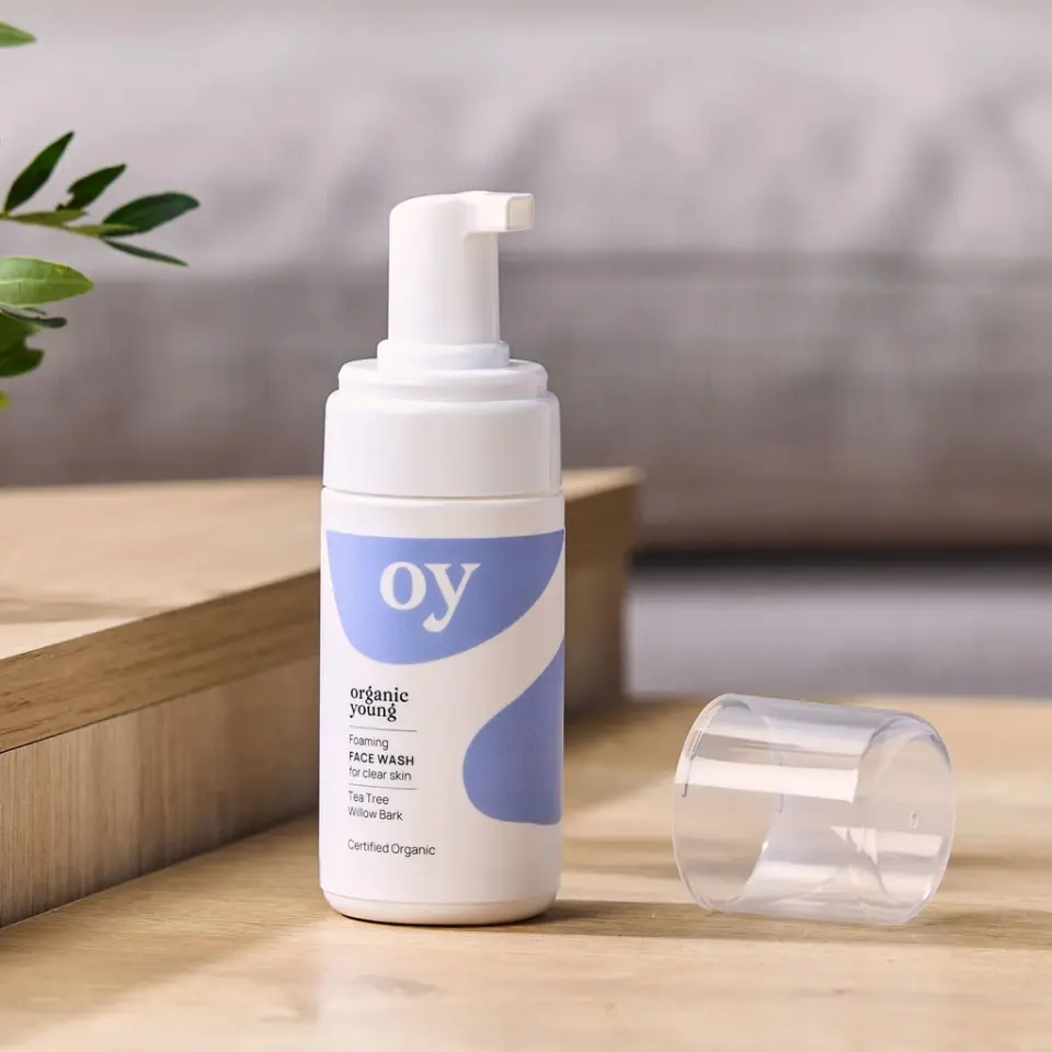 Organic Young foaming face wash on wooden surface, cap off, with plant in background.