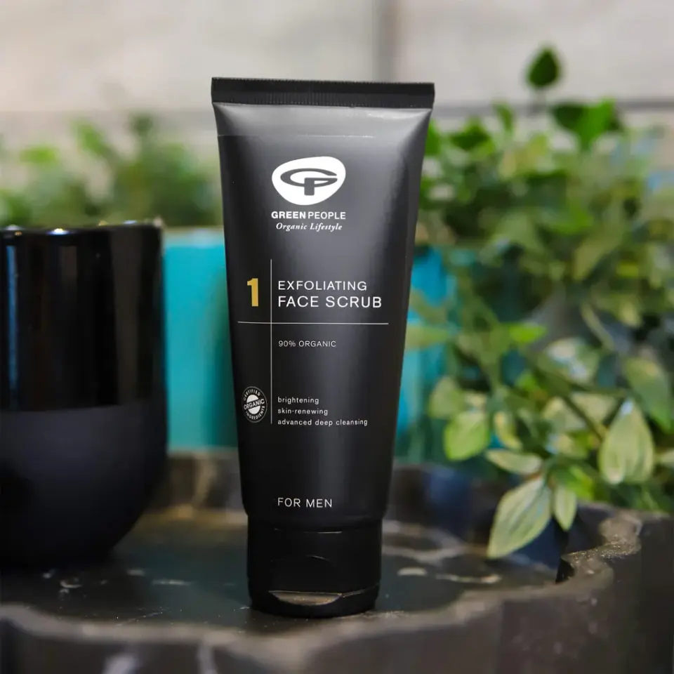 Black tube of Green People exfoliating face scrub for men, 90% organic, on a table with plants.