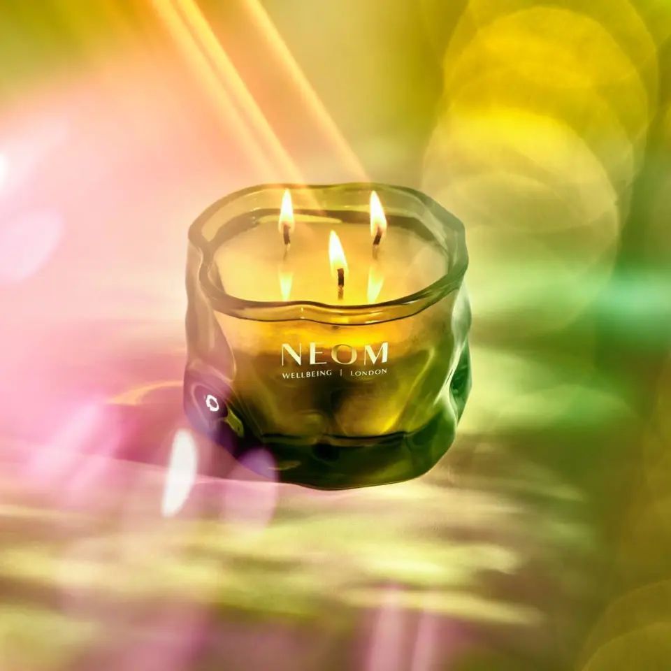Green glass candle with three flames, labelled "NEOM Wellbeing London" against a colourful background.